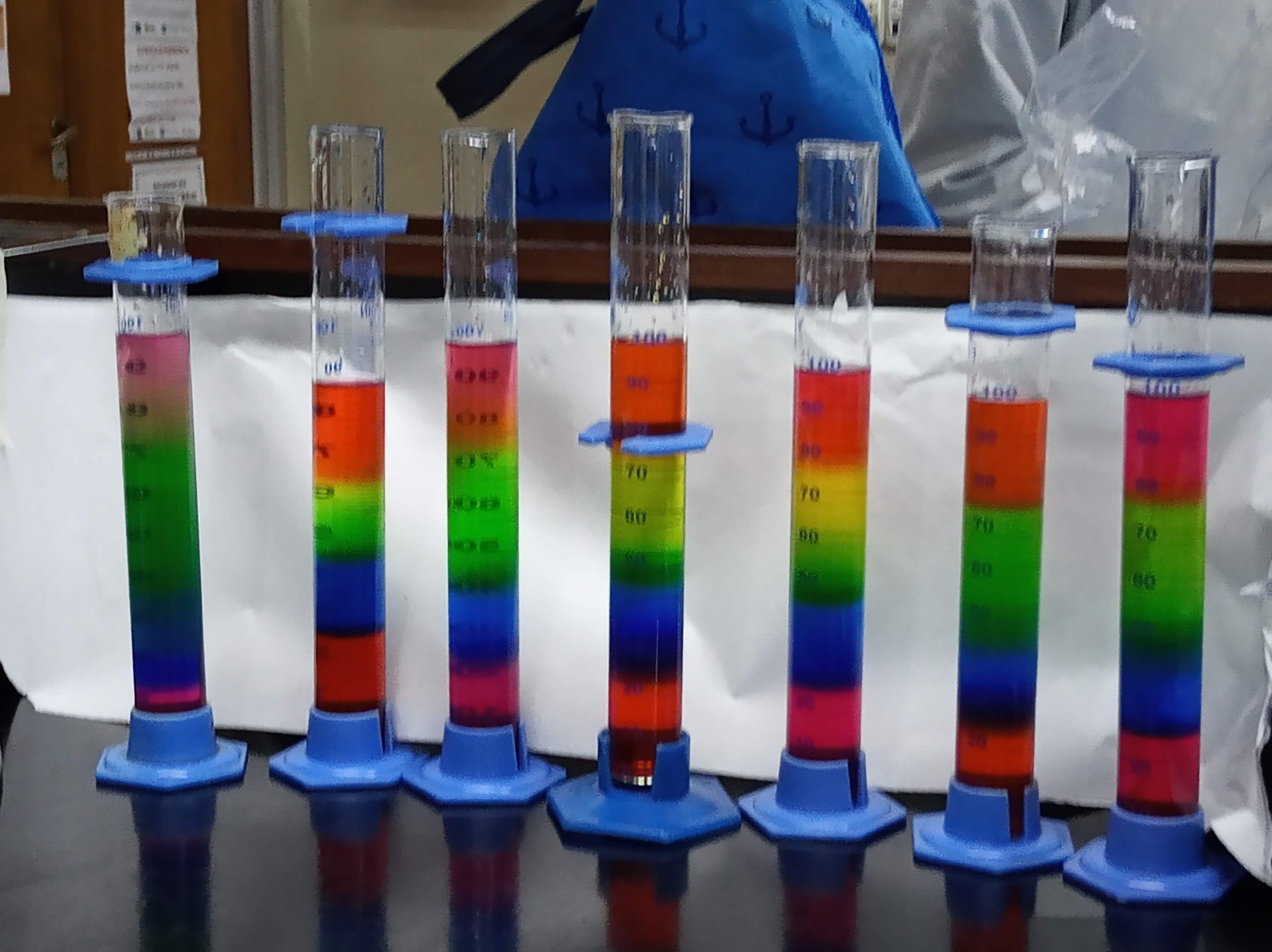 Sette cilindri graduati con liquidi disposti in strati colorati