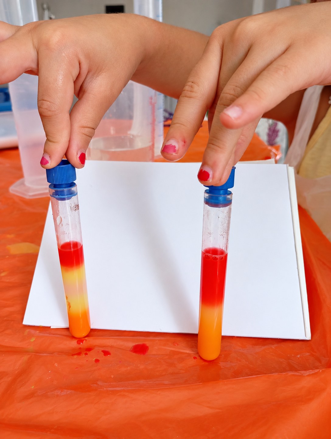 Mani di bambini tengono due provette con liquidi rossi, gialli e arancioni